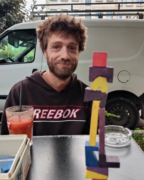 Clem, attablé en terrasse, devant une tour de blocs en bois qui tient encore debout